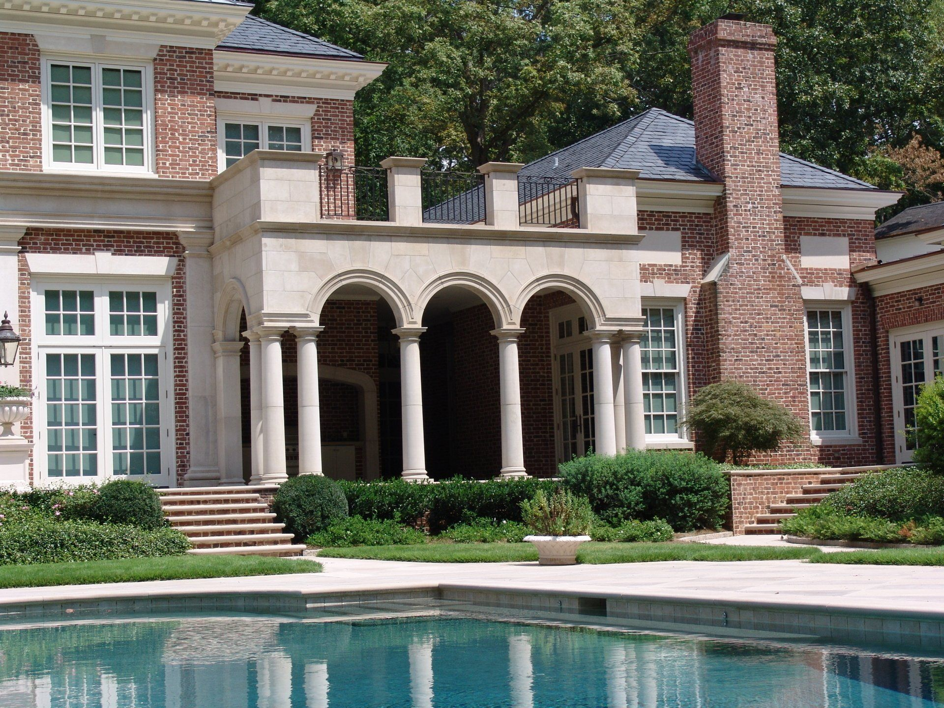 Luxury home with pool, red brick, white columns, and manicured landscaping.