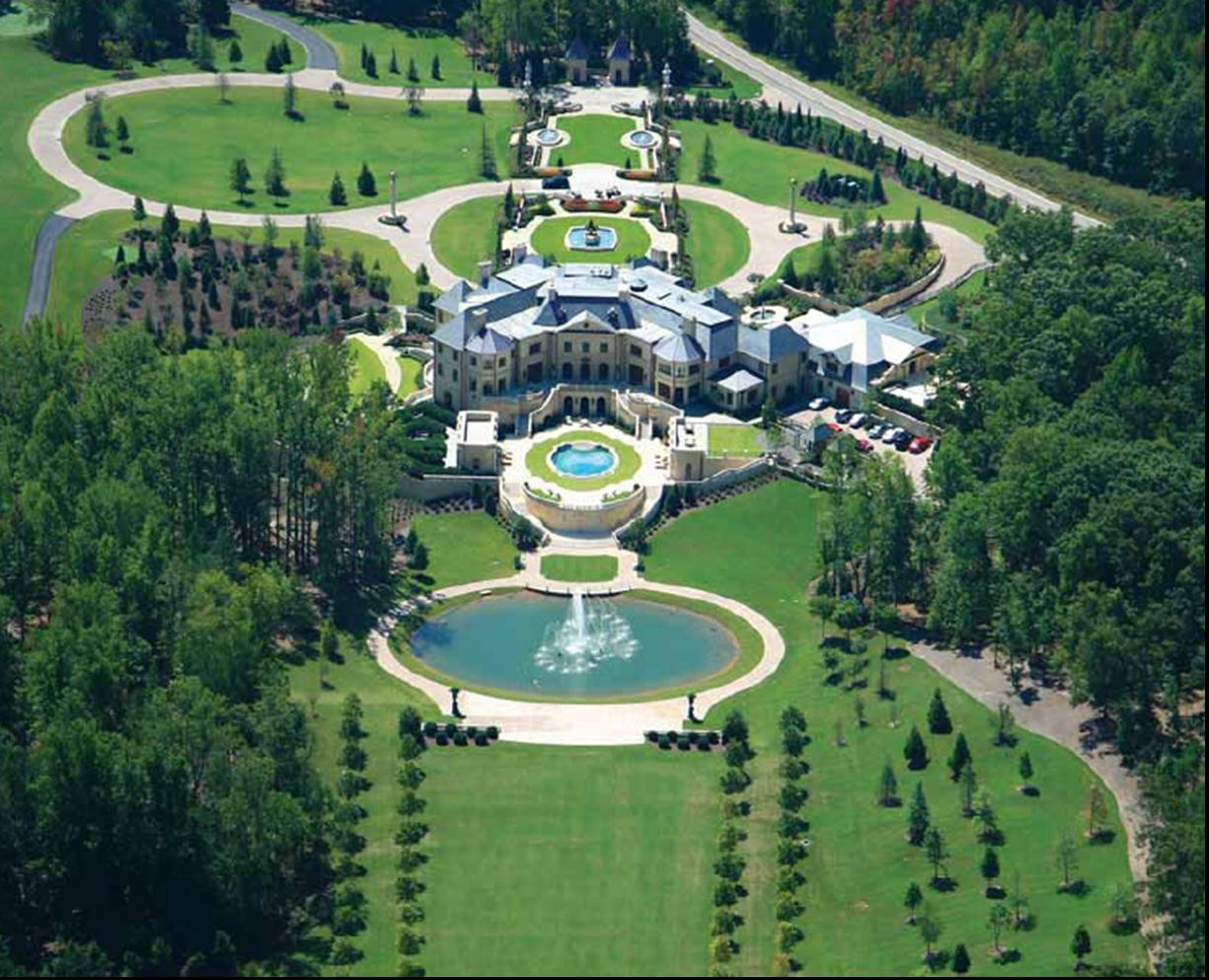 Aerial view of a large mansion with landscaped grounds, ponds, and fountains.