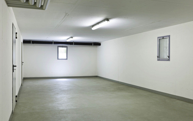 Empty, bright, white-walled garage with a concrete floor, lights, small window, and a door.