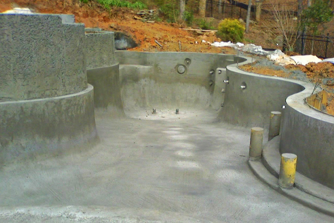 Concrete pool under construction; gray, curvy shape with holes, set outdoors on a hillside.