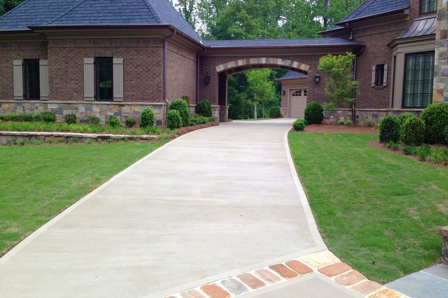 Long concrete driveway leading to brick home, connecting to a covered archway and garage. Green lawn on both sides.