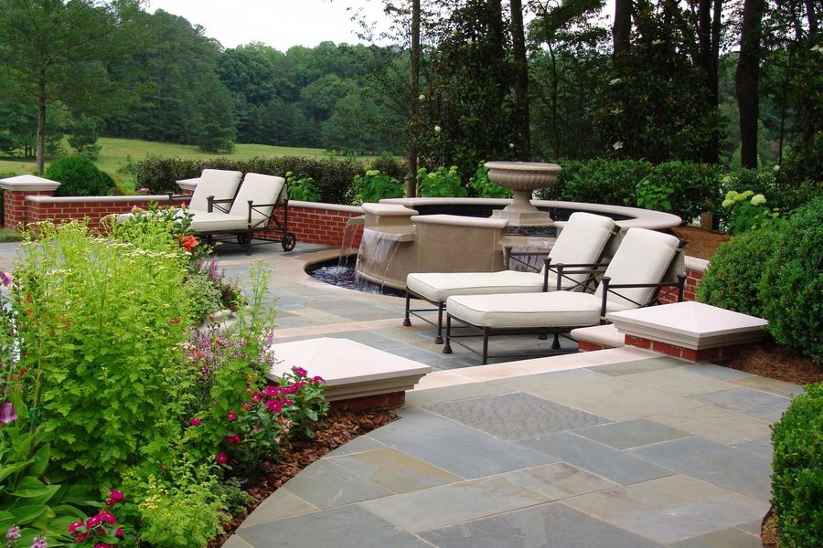 Patio with lounge chairs, fountain, brick walls, and lush garden in a natural setting.