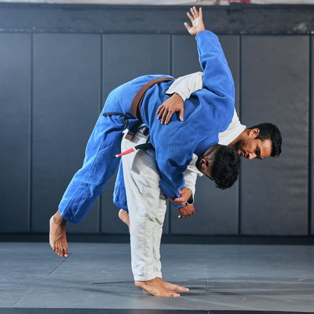 Two men grappling on a mat, one in blue, the other in black.