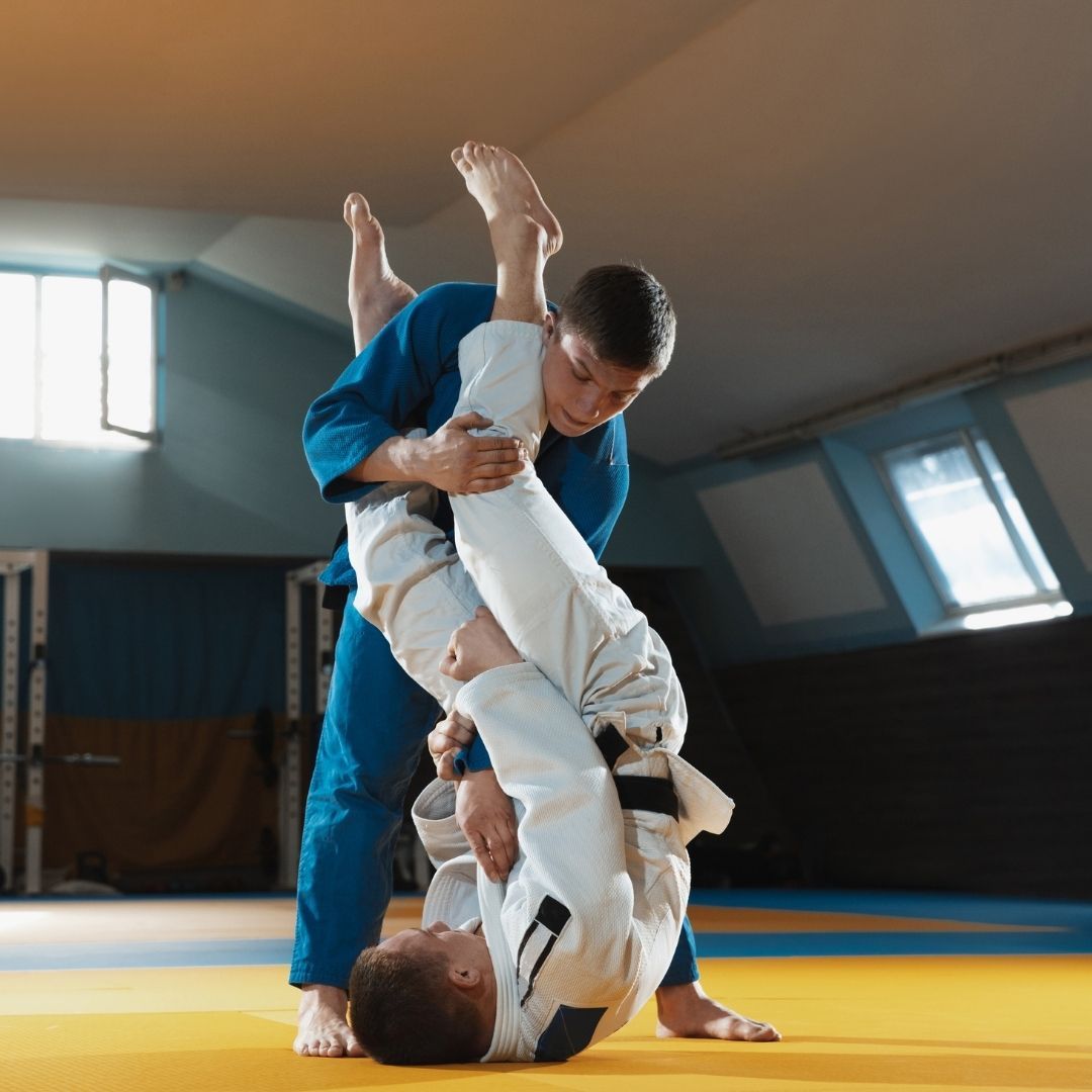 Five people in jiu-jitsu gear pose together in a gym.  Smiling,  some have arms around each other. Machado logo visible.