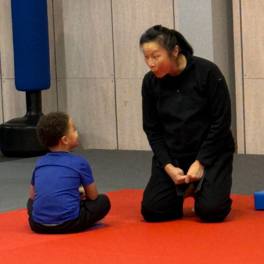 People practicing Brazilian Jiu-Jitsu. One person on the ground, another on top; two others grappling nearby. Black gis, indoor setting.