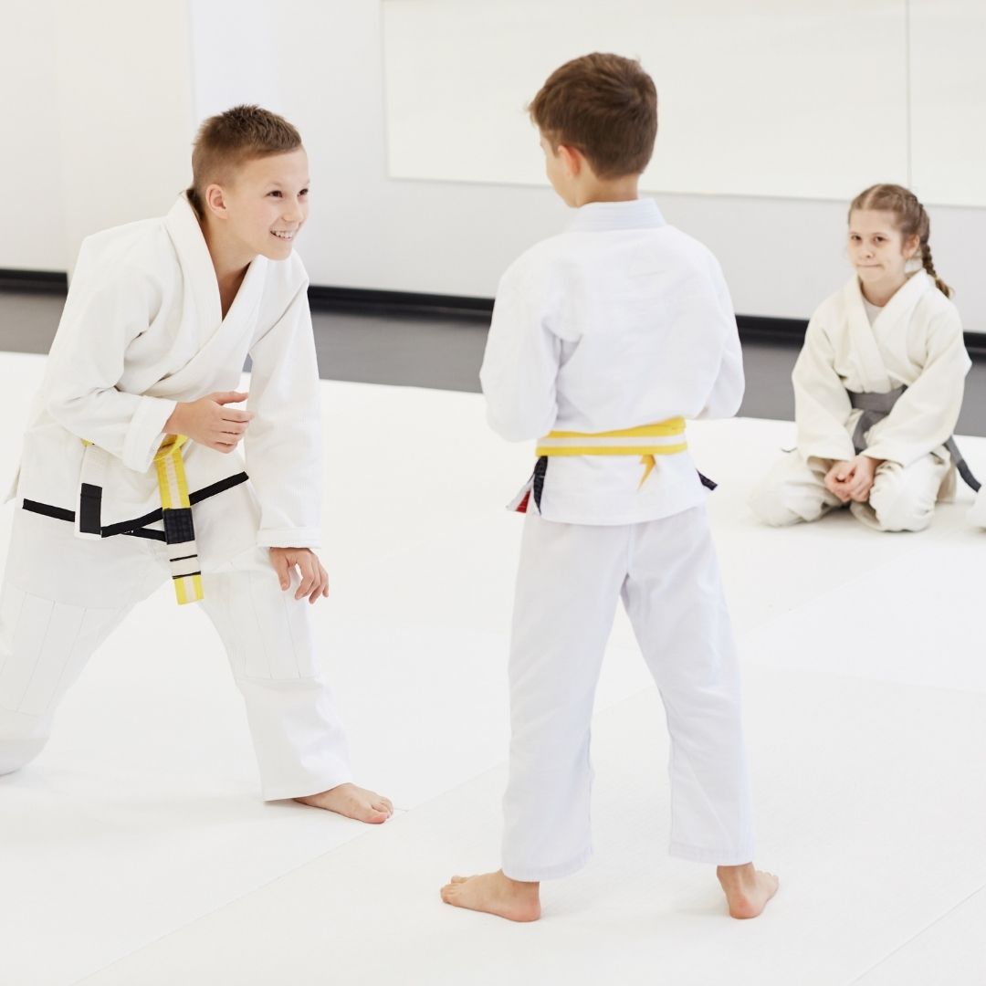 Two people grappling on a mat, one in a black gi, the other in a rash guard, legs entangled.