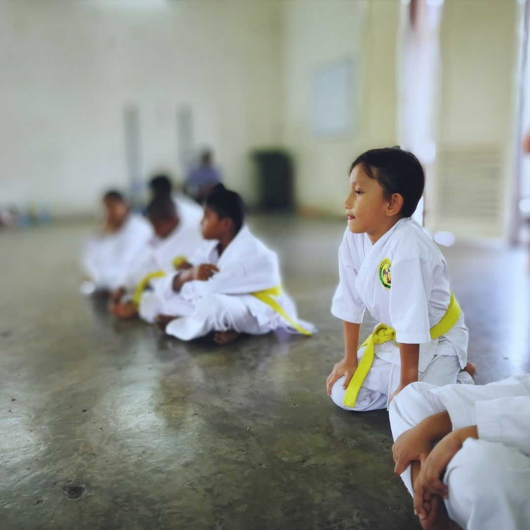 Two children in black and white martial arts uniforms practice a chokehold on a mat. One child smiles.