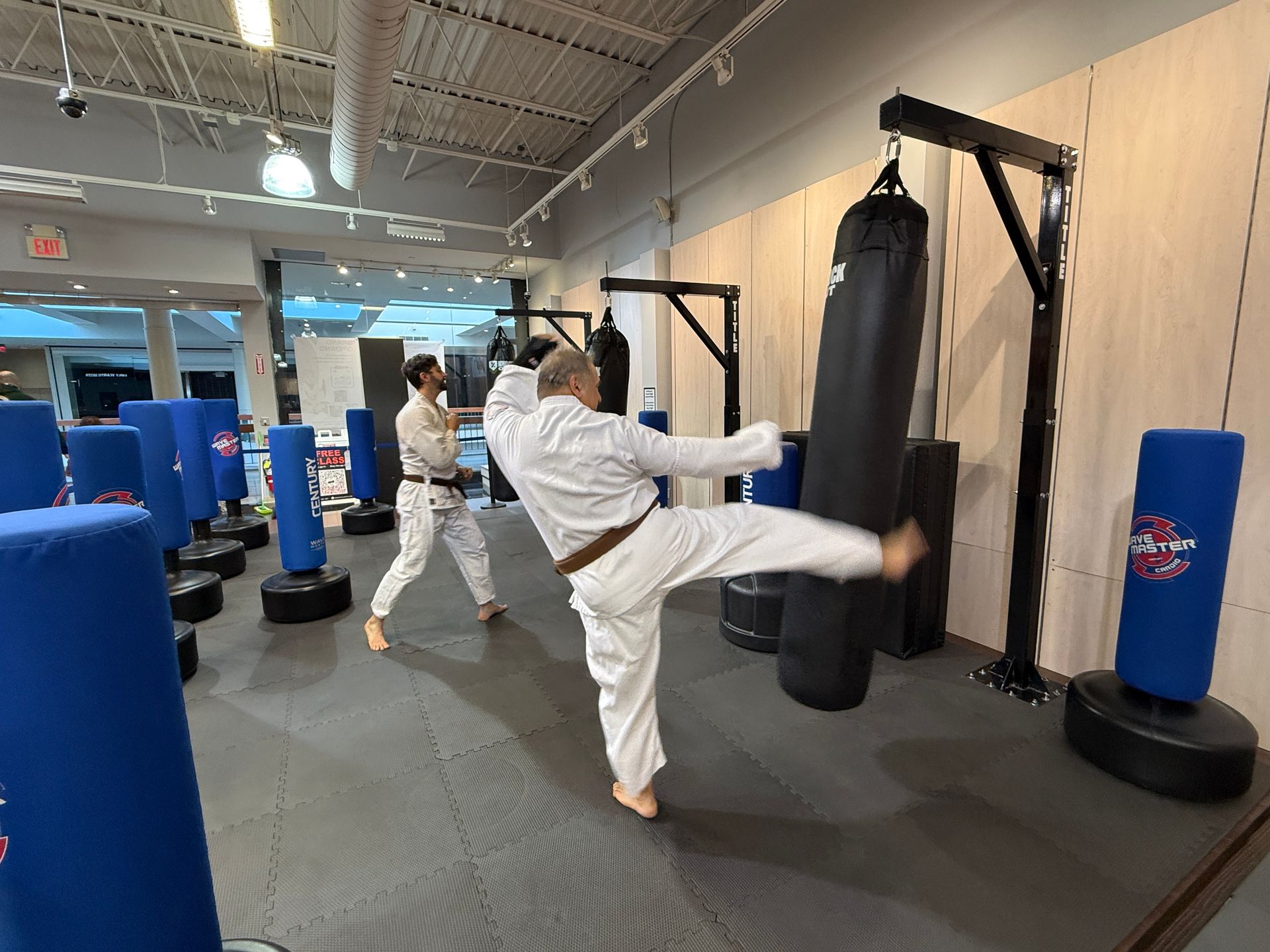 Two people practicing Brazilian Jiu-Jitsu on a mat; one in a black gi, one in a white gi, grappling.