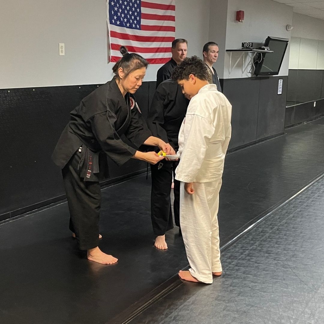 Two boys on a mat practicing Jiu-Jitsu. One boy is on top, giving a thumbs-up.