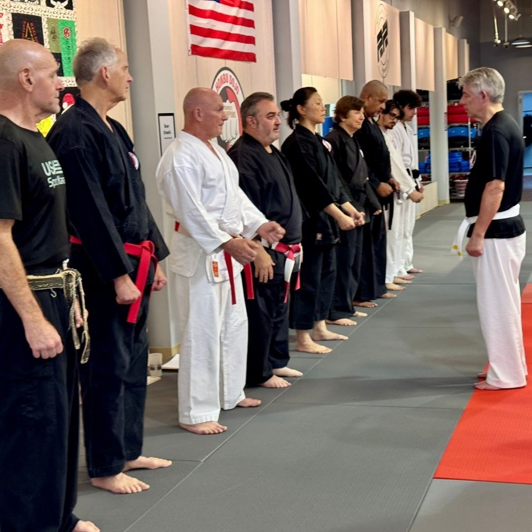 Five people in jiu-jitsu gear pose together in a gym.  Smiling,  some have arms around each other. Machado logo visible.