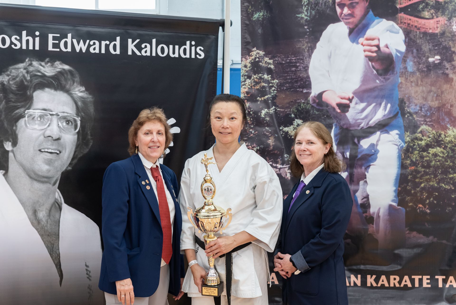 Group of children in martial arts attire posing, some with arms around each other, in a gym.