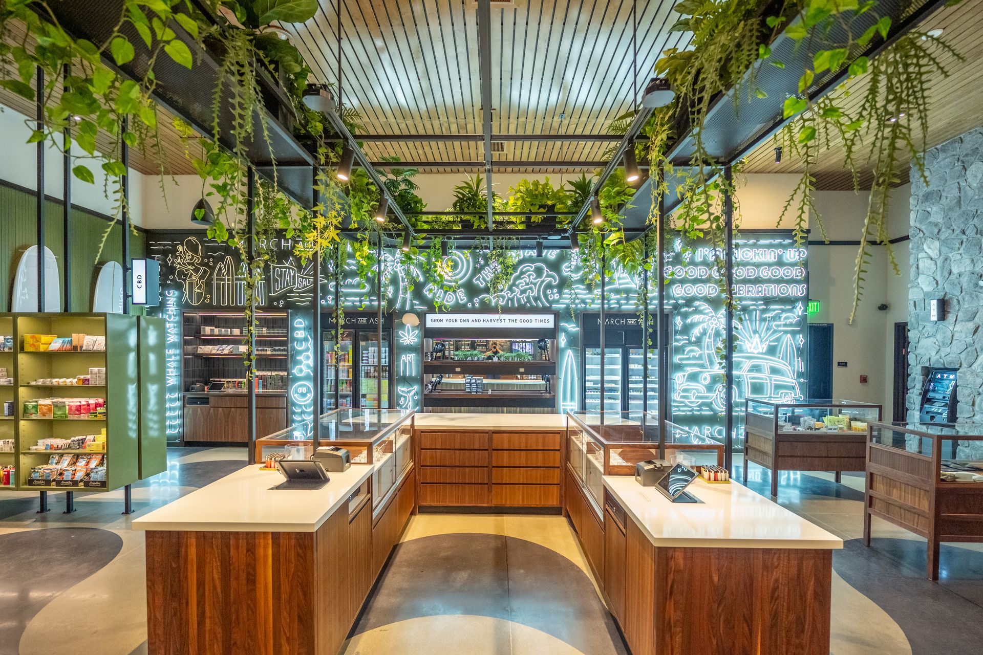 Interior of a modern retail space, likely a dispensary, with wood and greenery accents, display cases.