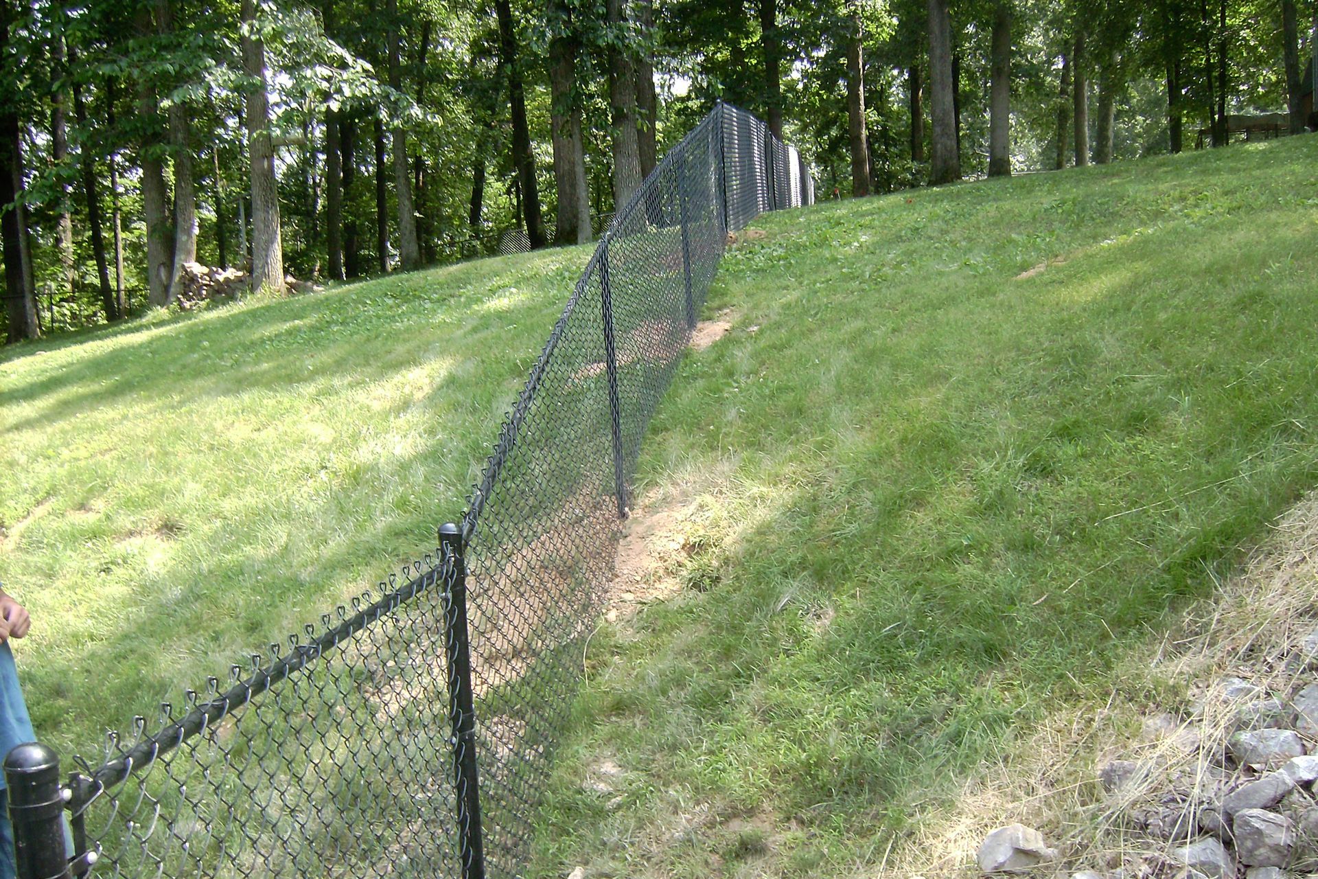 A chain link fence is sitting on top of a lush green hillside.