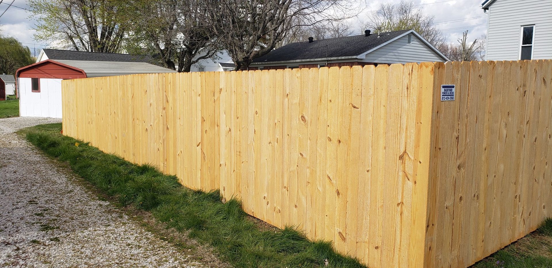 A wooden fence is sitting on the side of a gravel road next to a house.