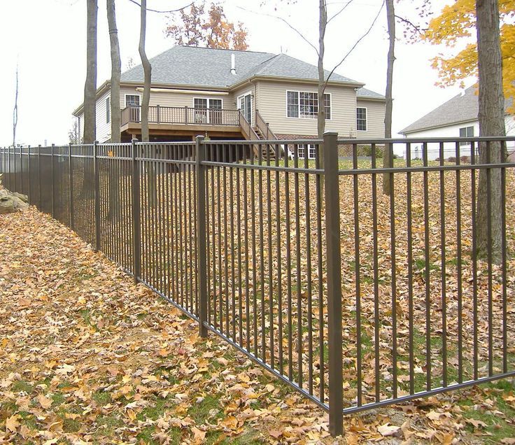 A metal fence surrounds a yard with a house in the background