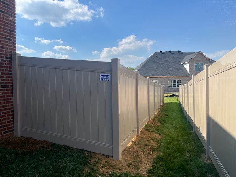 A white vinyl fence surrounds a grassy yard in front of a brick house.