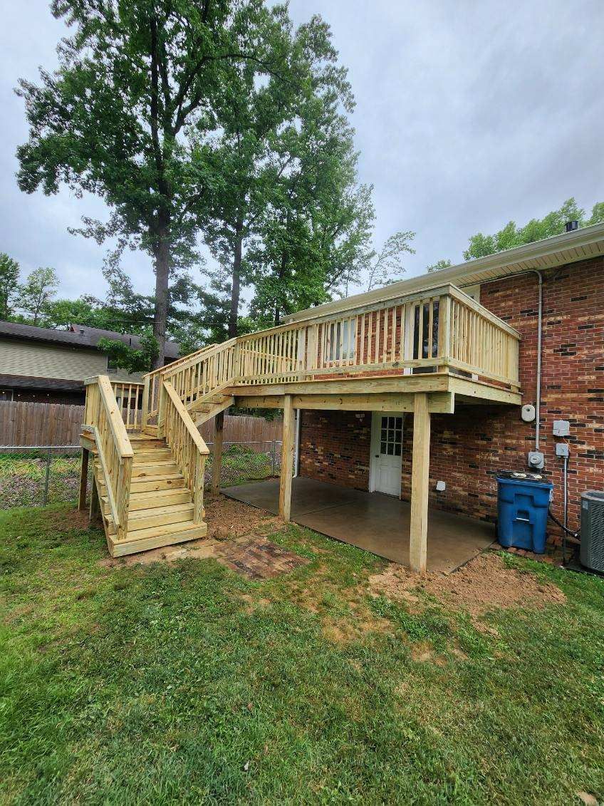 A wooden deck with stairs leading up to it is in the backyard of a house.