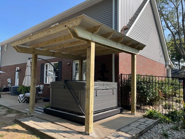 A hot tub is under a wooden pergola in front of a house.