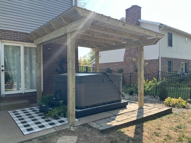 A hot tub is sitting under a wooden pergola on a patio.