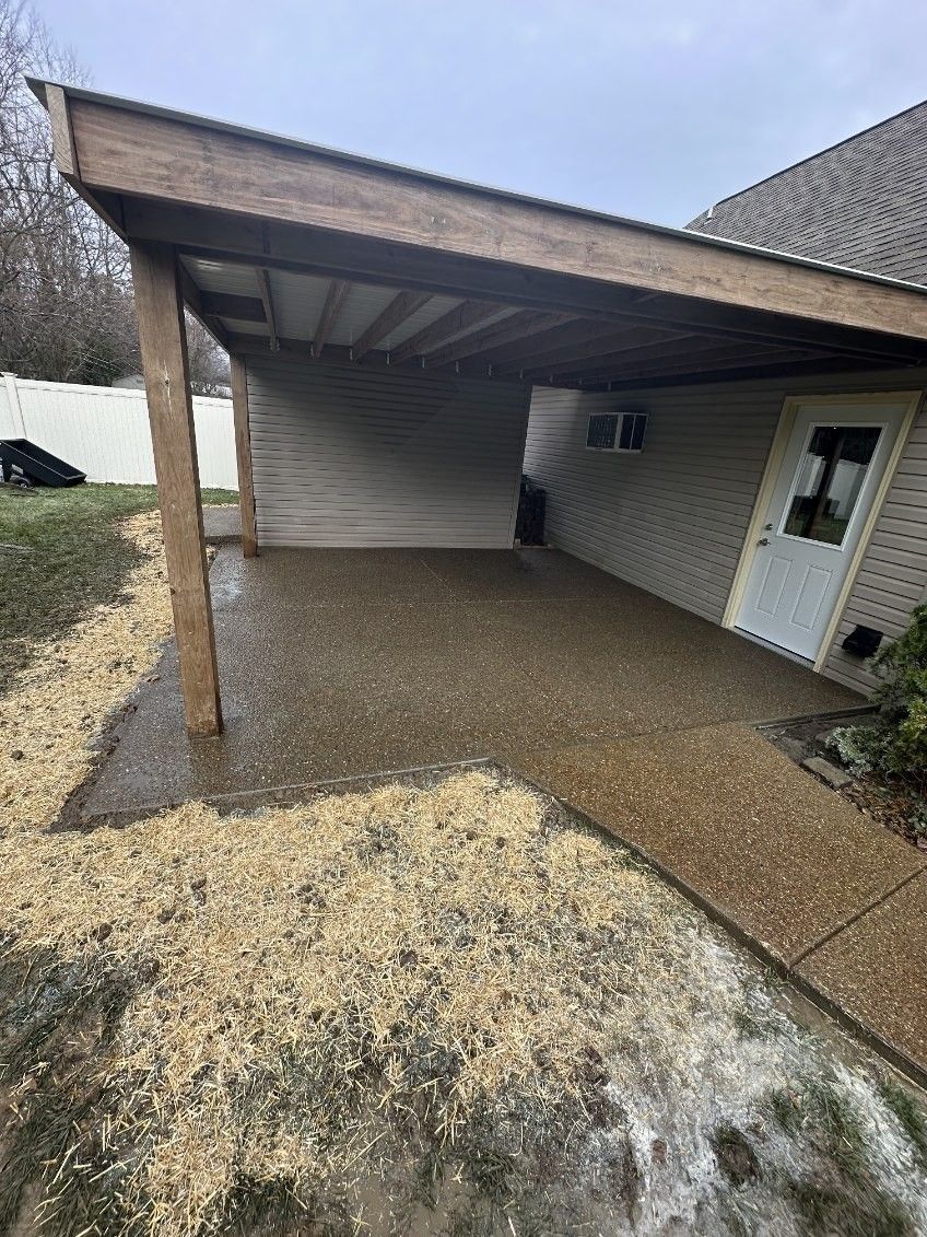 A carport with a wooden roof and a concrete walkway in front of a house.
