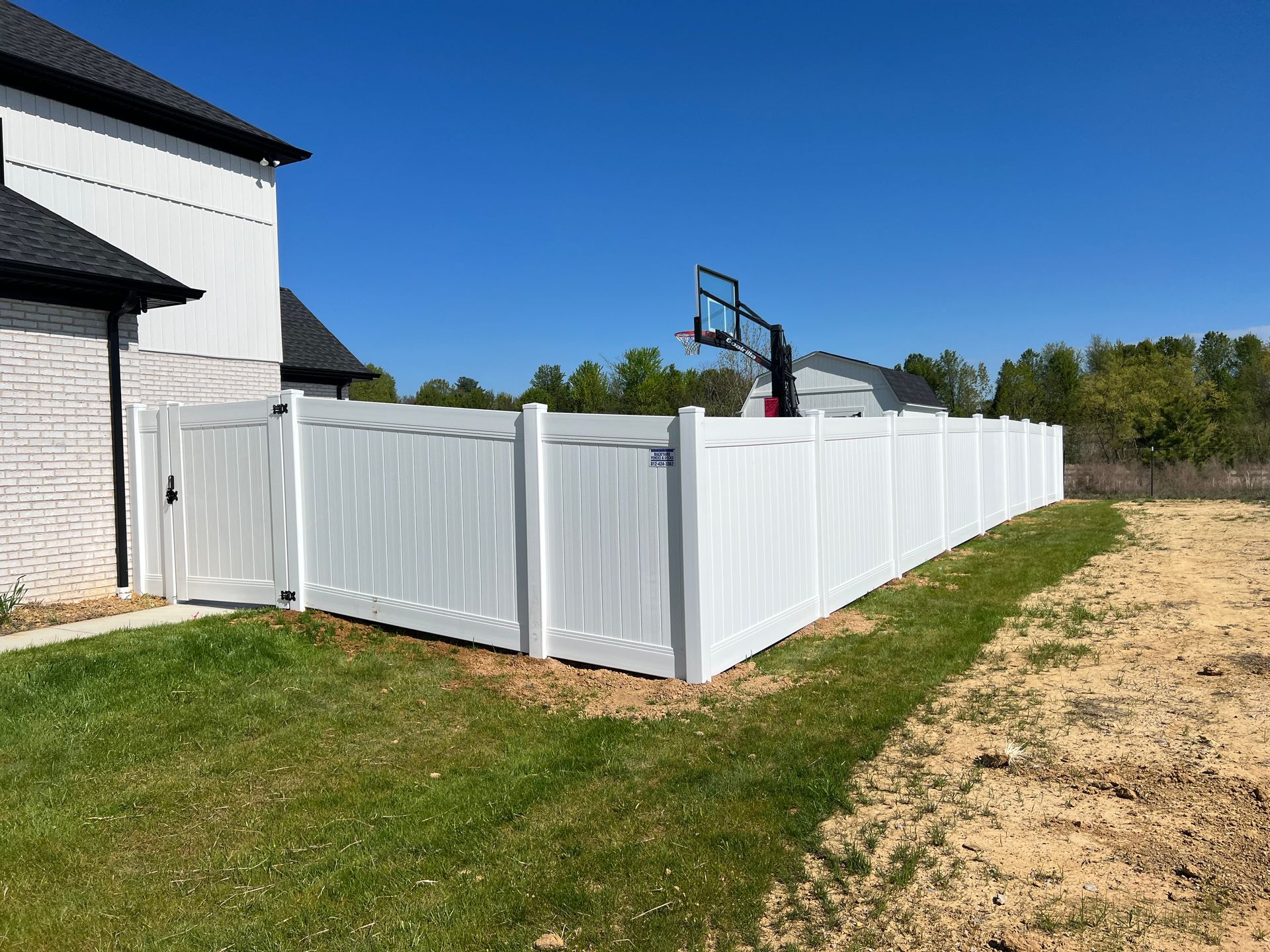 A white fence with a basketball hoop in the backyard of a house.