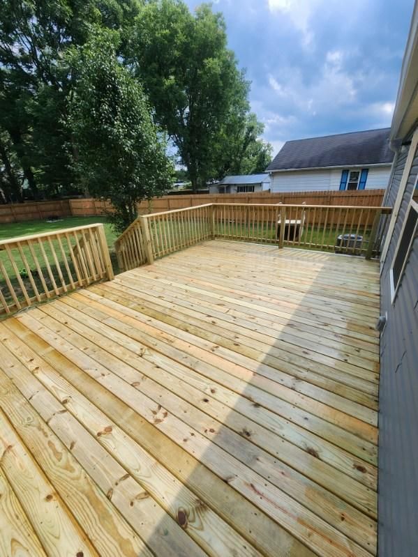 A large wooden deck with a fence around it and a house in the background.