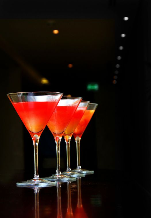 Four vibrant red cocktails in martini glasses lined up on a reflective dark surface.