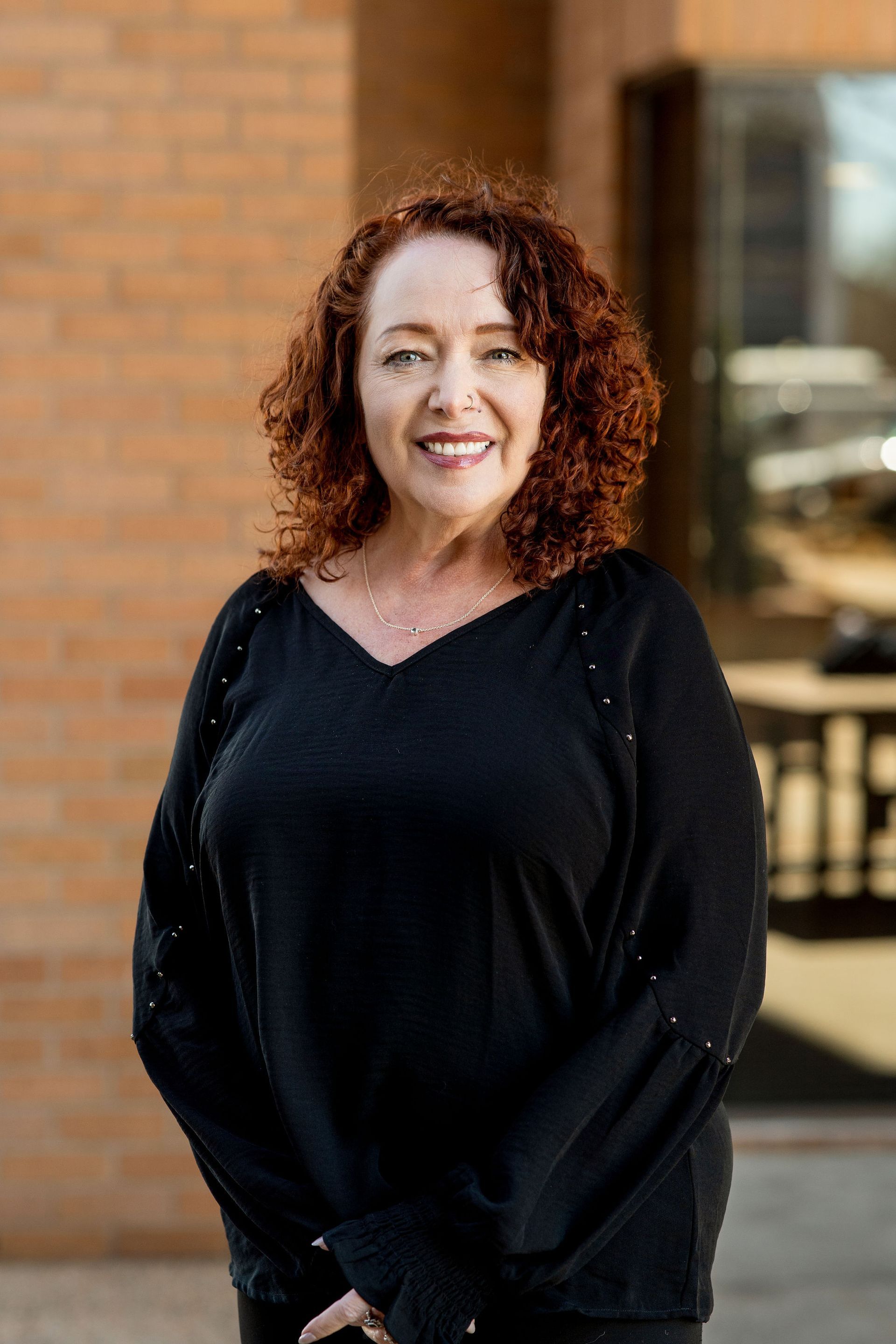 A woman with red hair is smiling and wearing a necklace.
