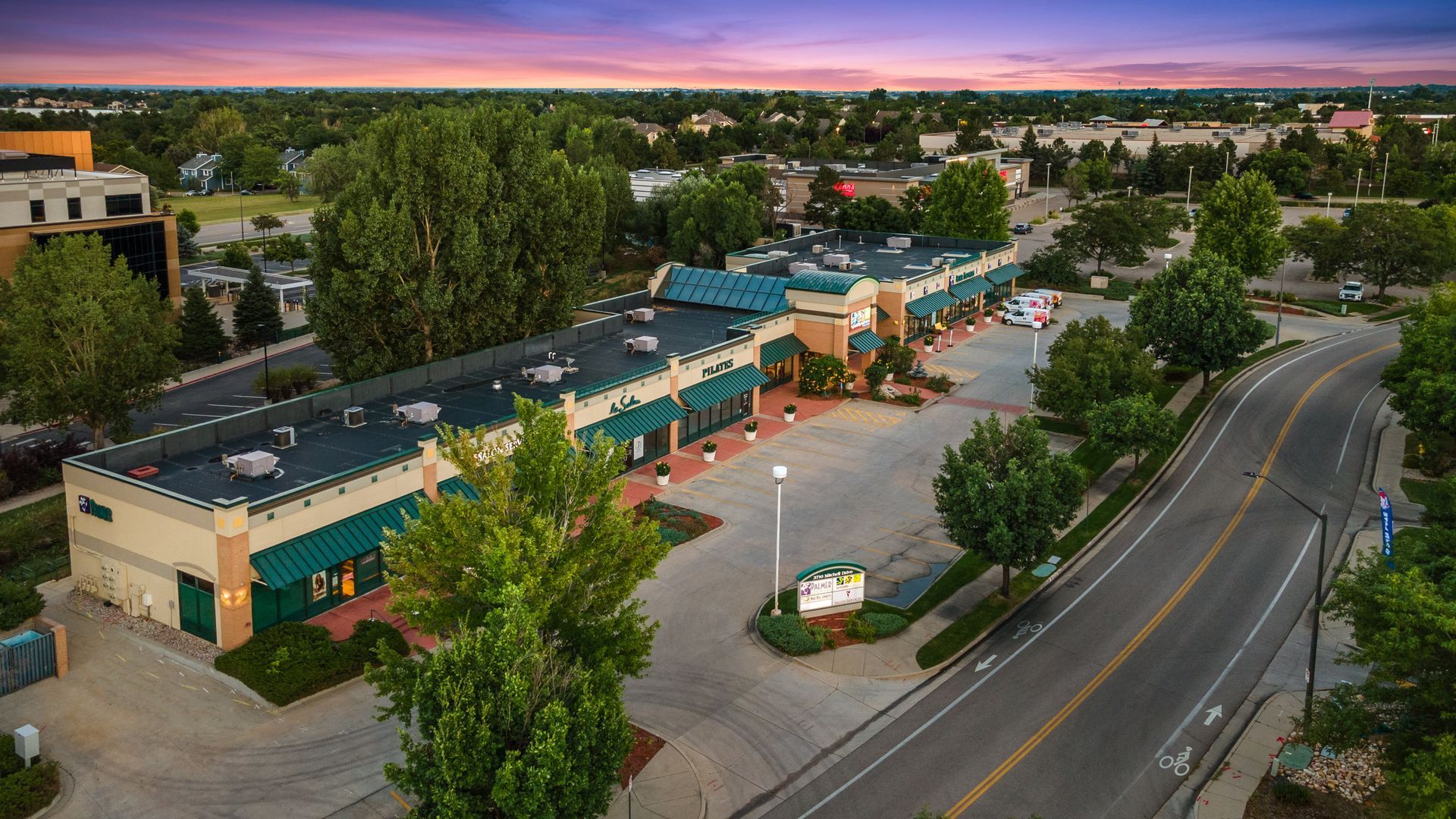 An aerial view of a large building surrounded by trees and a road.