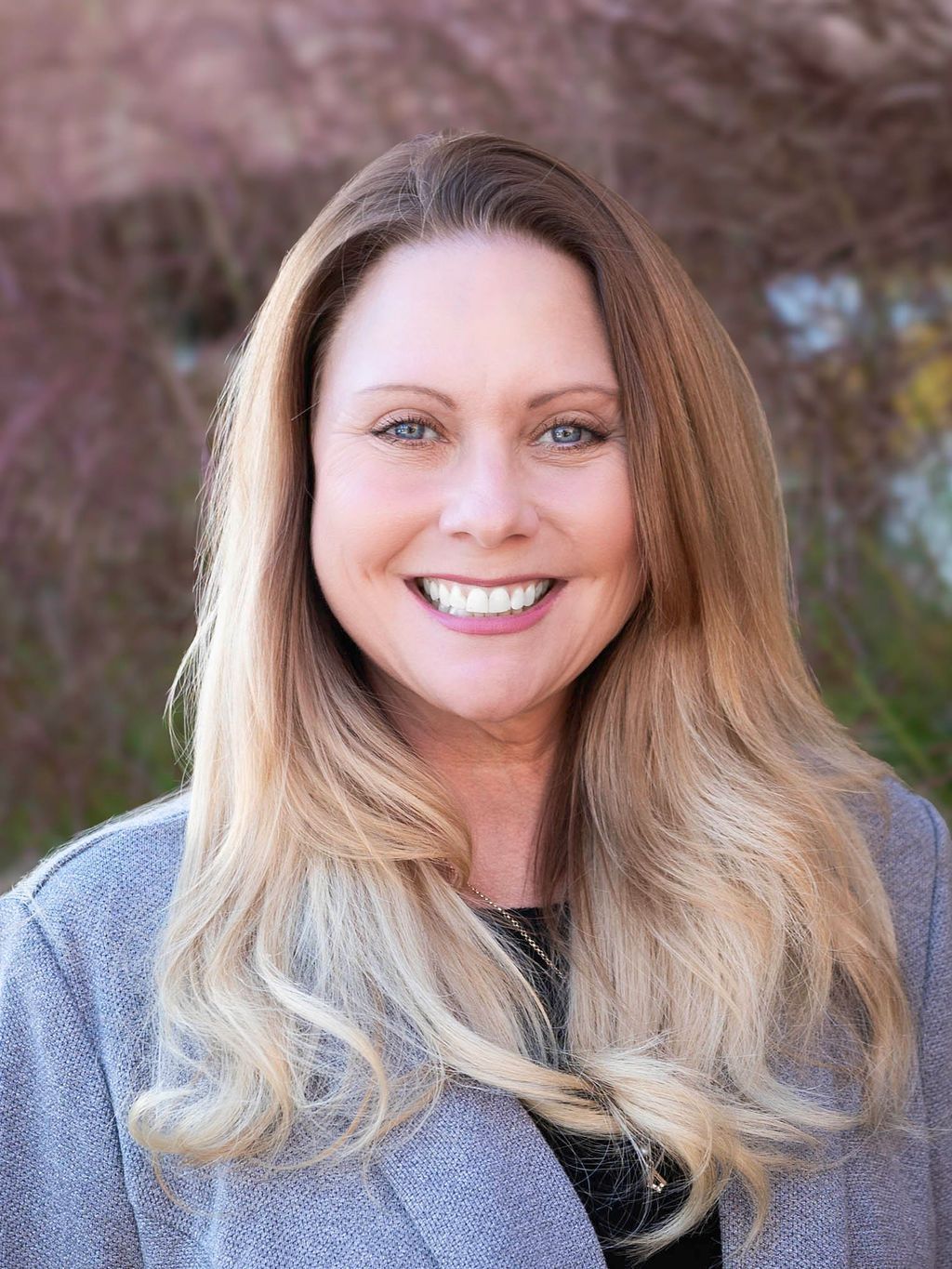 A woman with long hair is wearing a blue shirt and smiling.