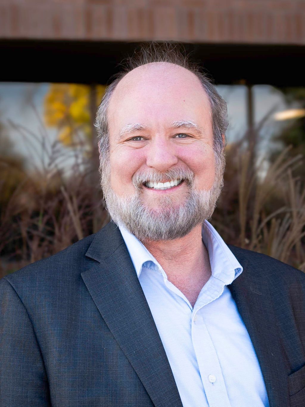 A man with a beard is wearing a red jacket and smiling.