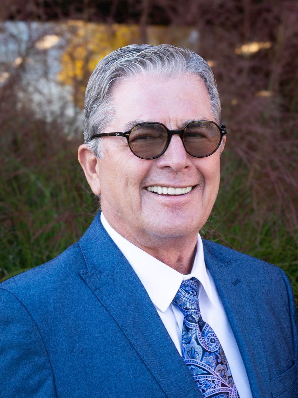 A man in a suit and white shirt is smiling in front of a window.