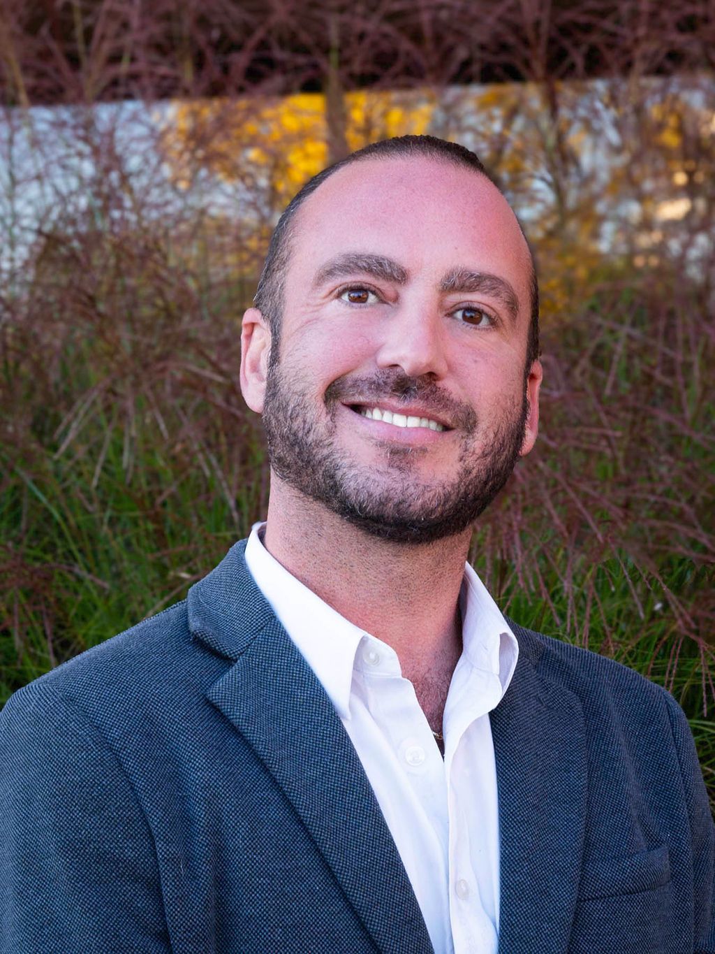 A man with a beard is wearing a suit and smiling for the camera.