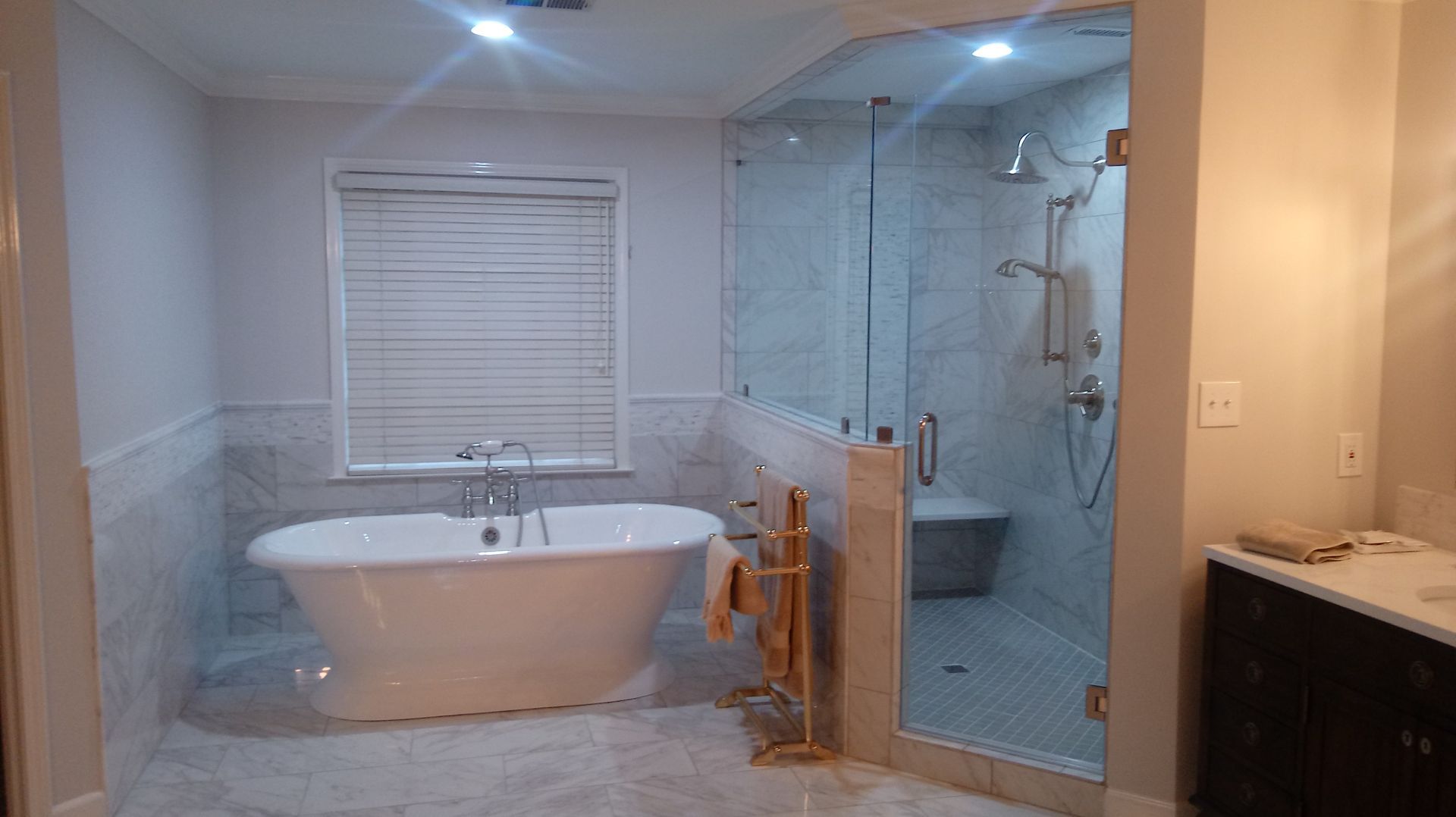 Modern bathroom with a white bathtub, glass shower, and gray tile.