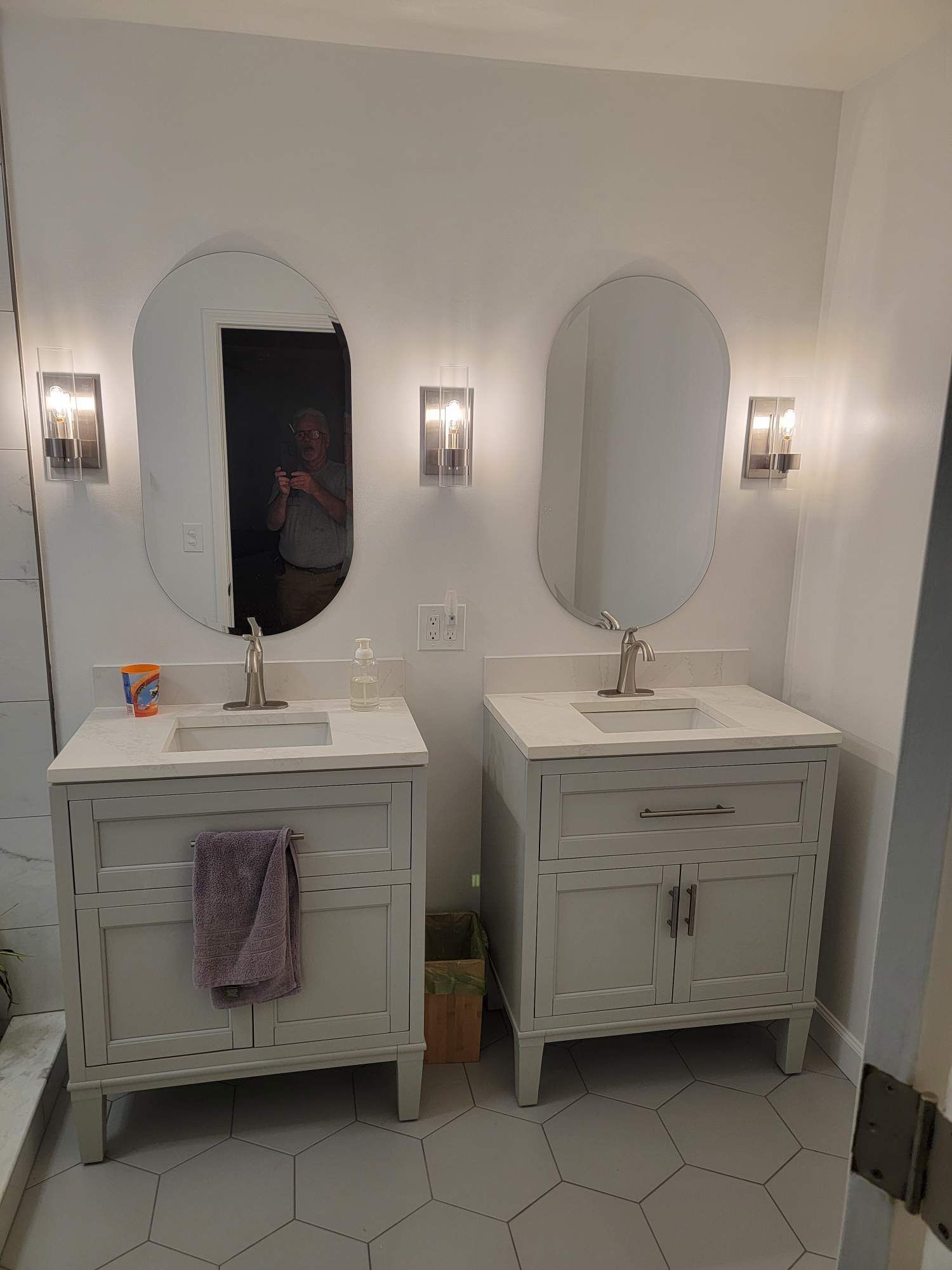 Bathroom with two white vanities, oval mirrors, and sconces.