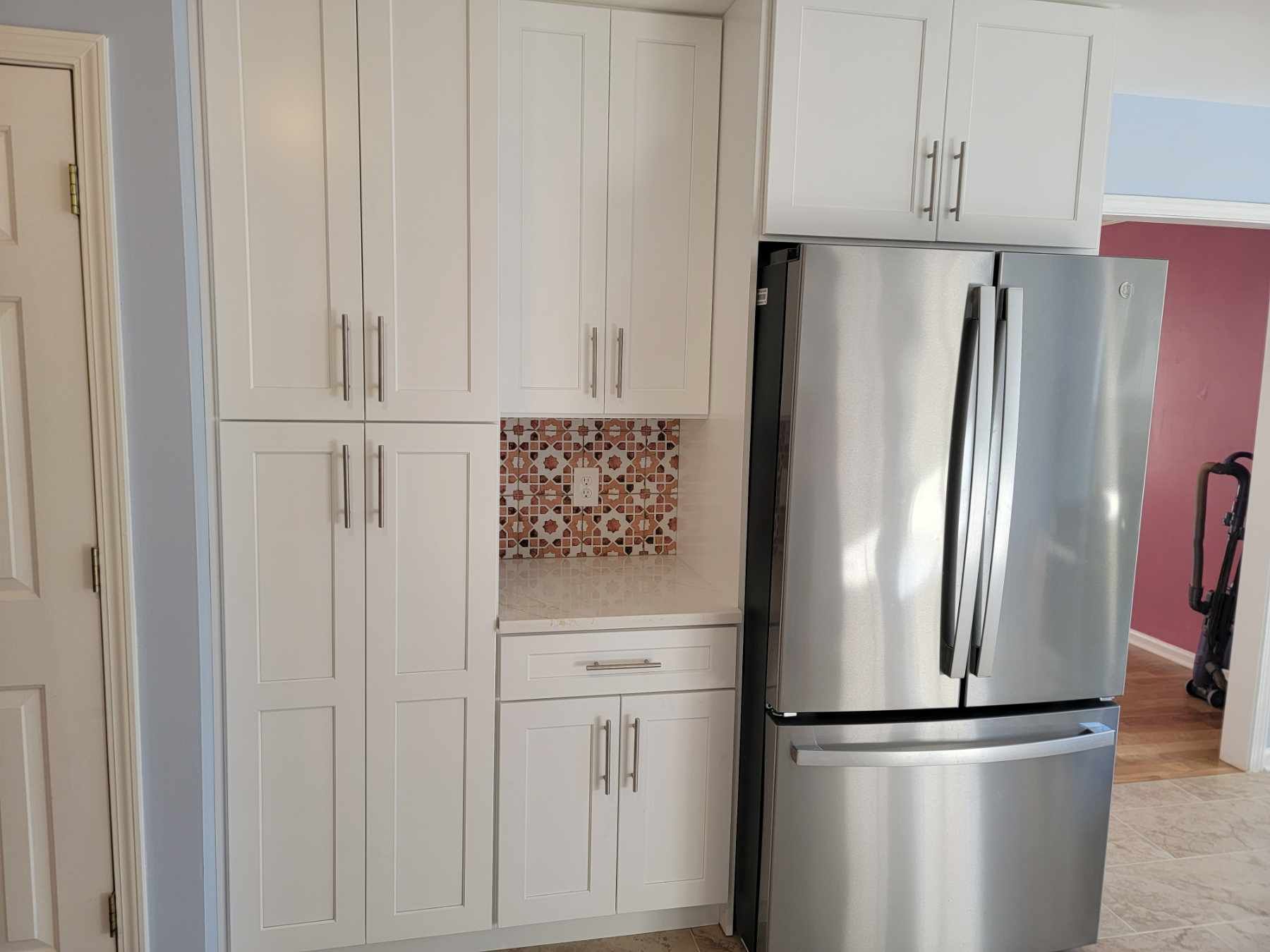 White kitchen cabinets next to a stainless steel refrigerator. Decorative tile backsplash.