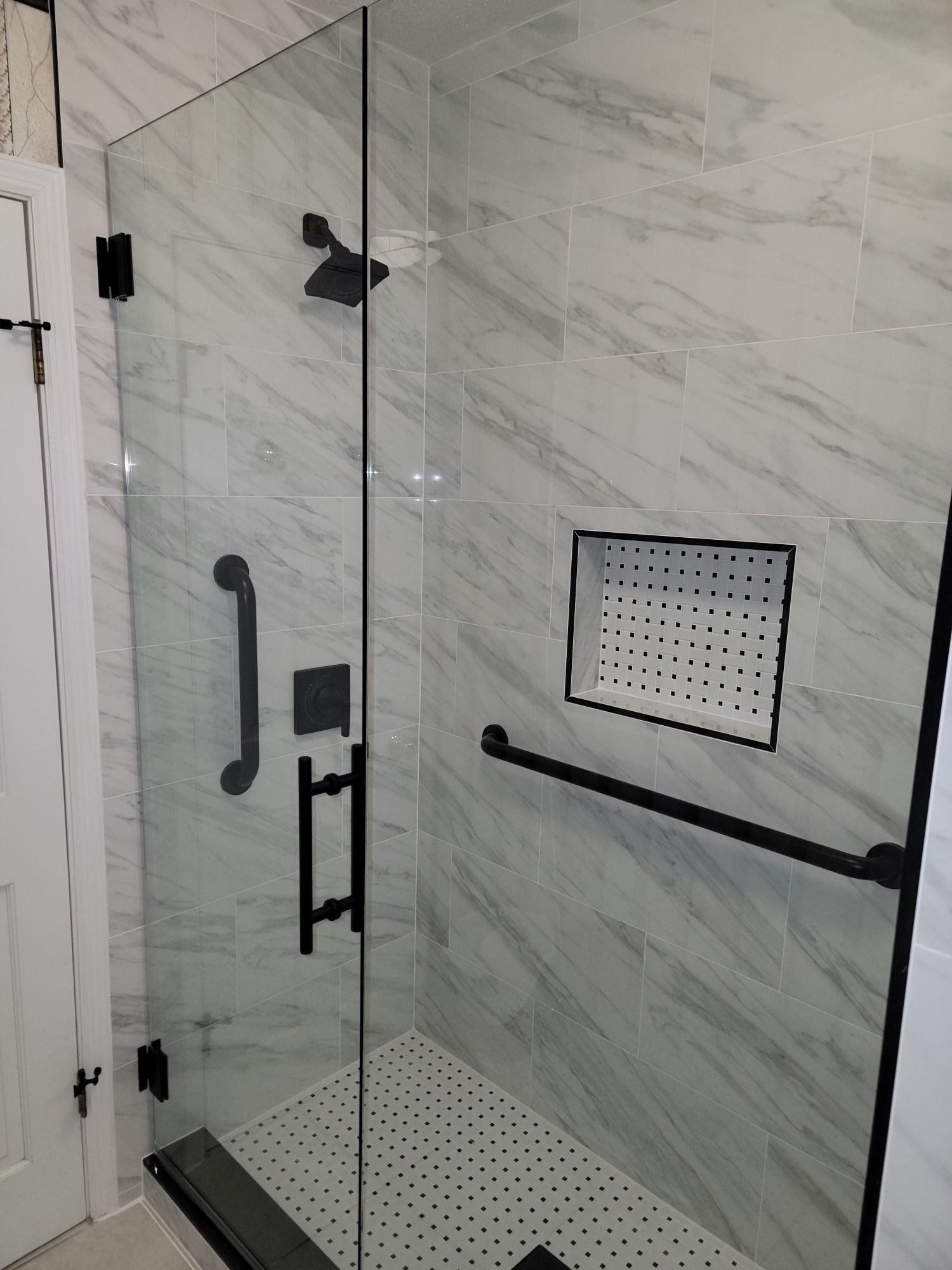 Glass shower enclosure with black hardware and marble-patterned tile walls.