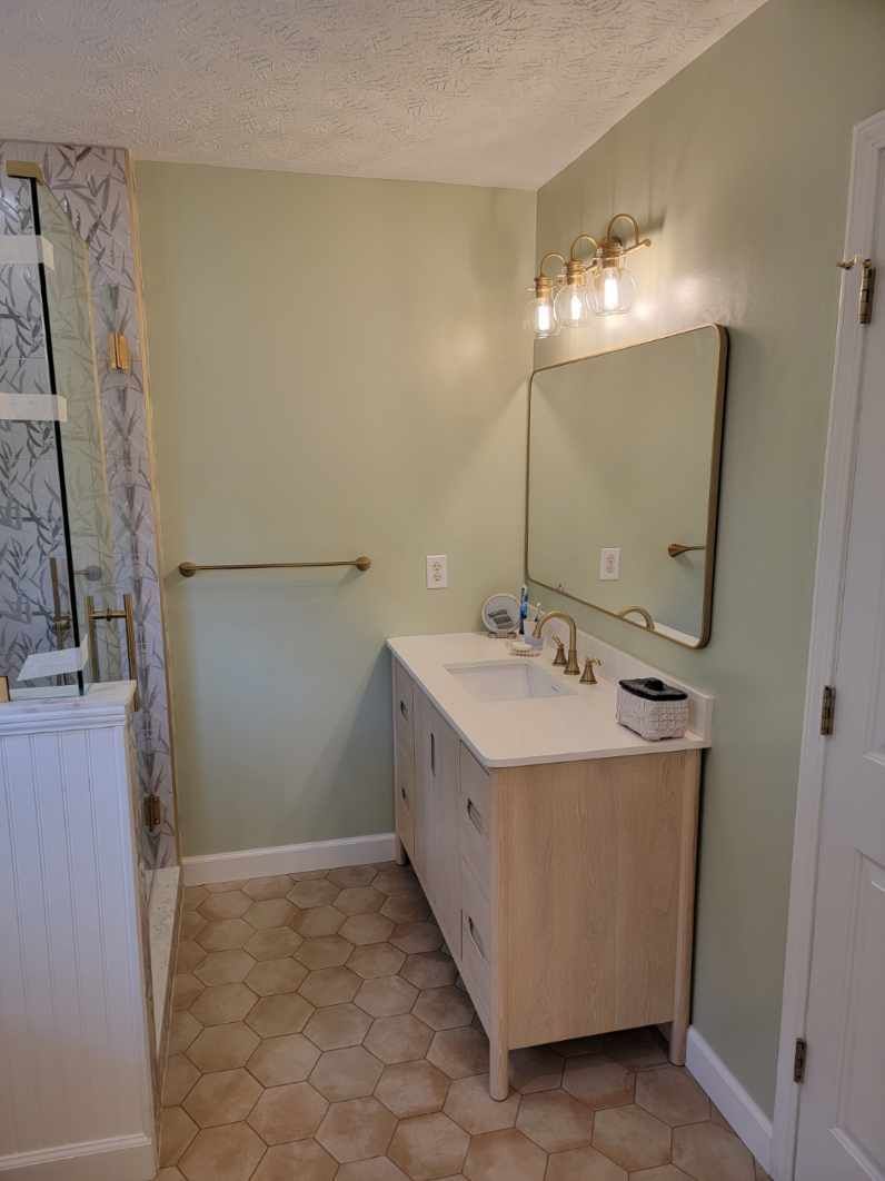 Bathroom with sage green walls, light wood vanity, and hexagon floor tiles.