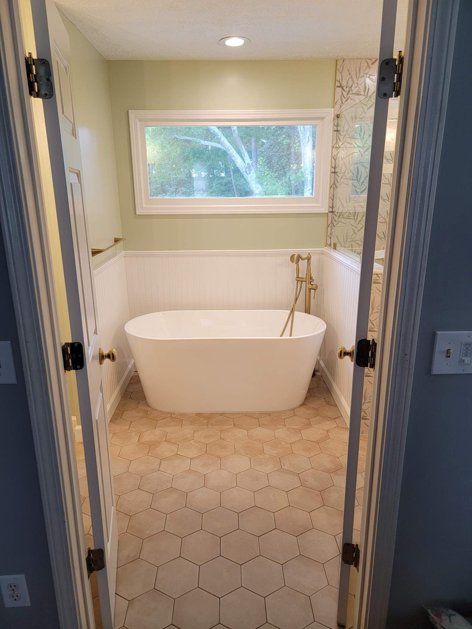 Bathroom with a white freestanding tub, hexagonal tile floor, and a window.