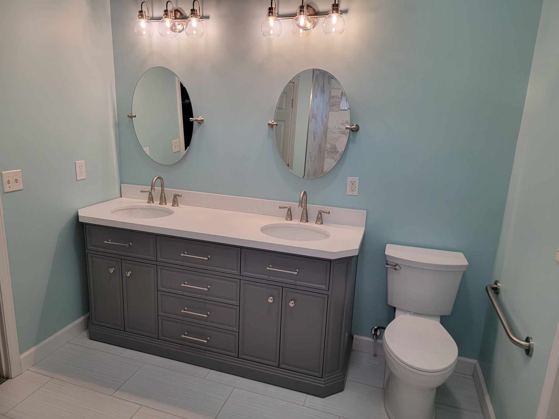 Bathroom with double sink vanity, oval mirrors, light blue walls, and toilet.