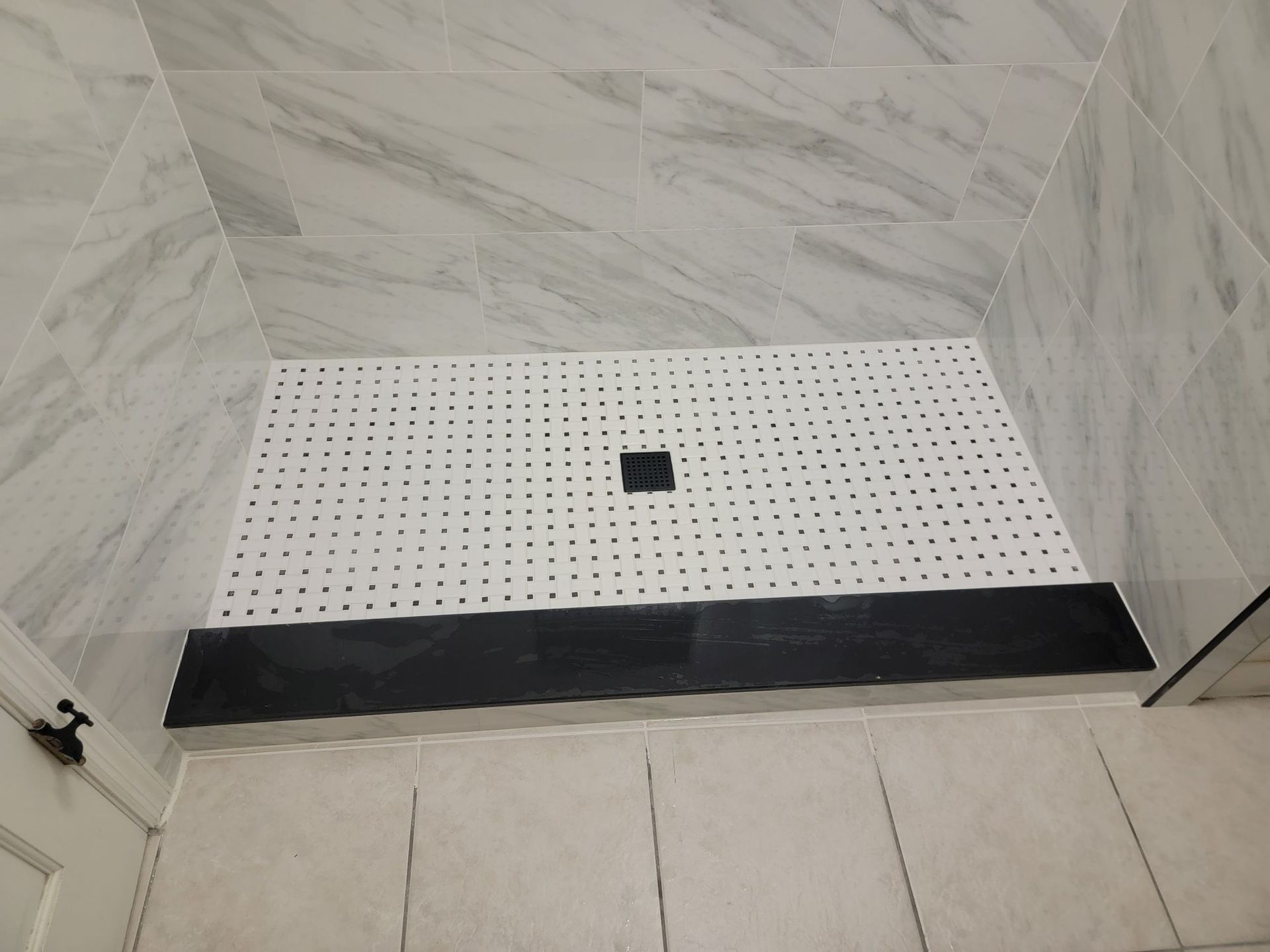 Shower with white tiled walls, black base, and a white, perforated floor.