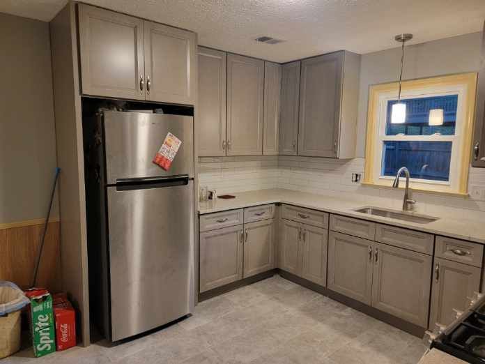 Kitchen renovation with gray cabinets, stainless steel fridge, and white countertops.