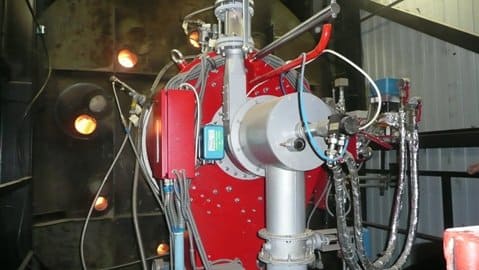 Ein roter Industriebrenner mit angebauten Komponenten. Silberne und blaue Elemente in einem dunklen Gehäuse.