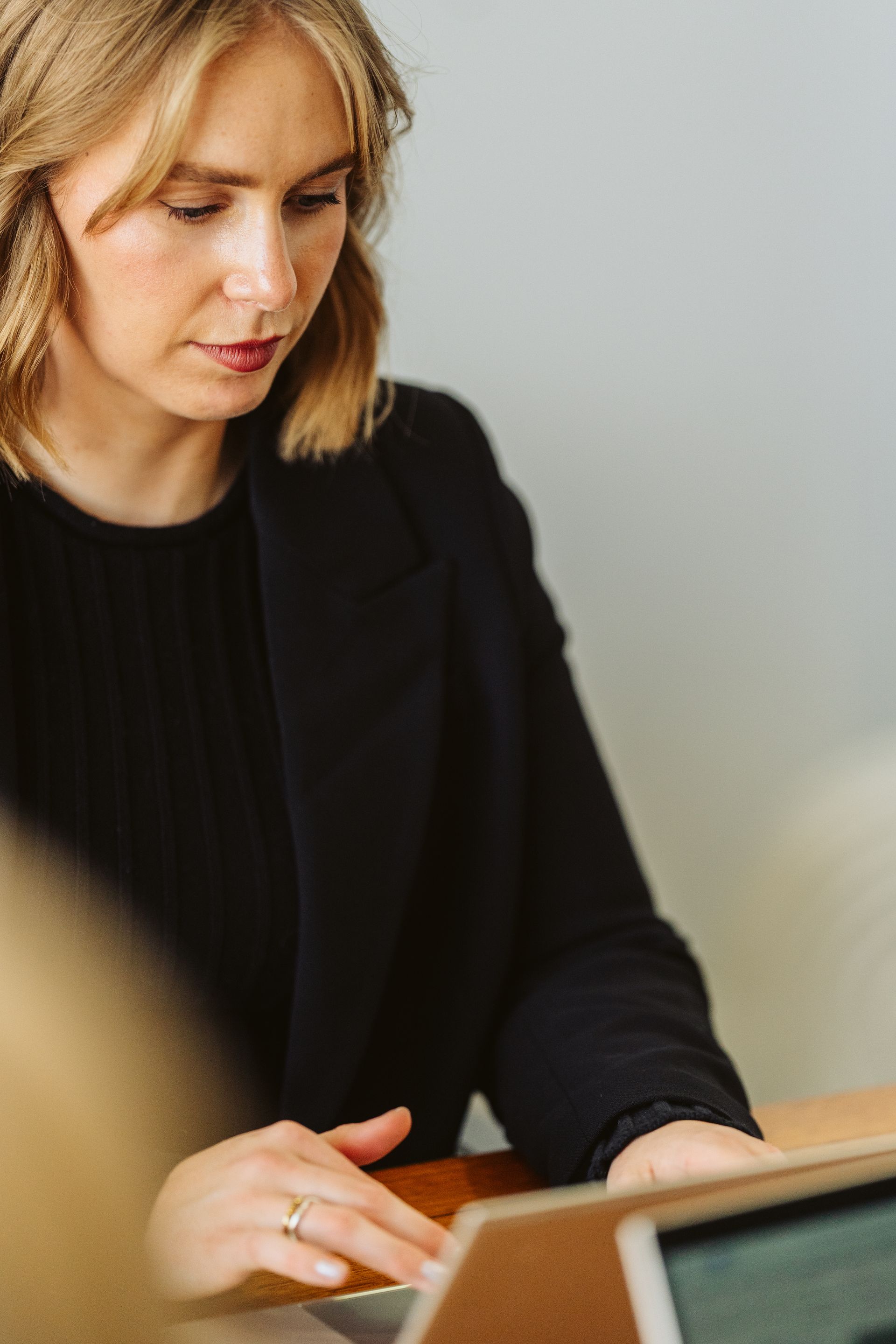 Woman in black blazer at a table, looking down, focused.