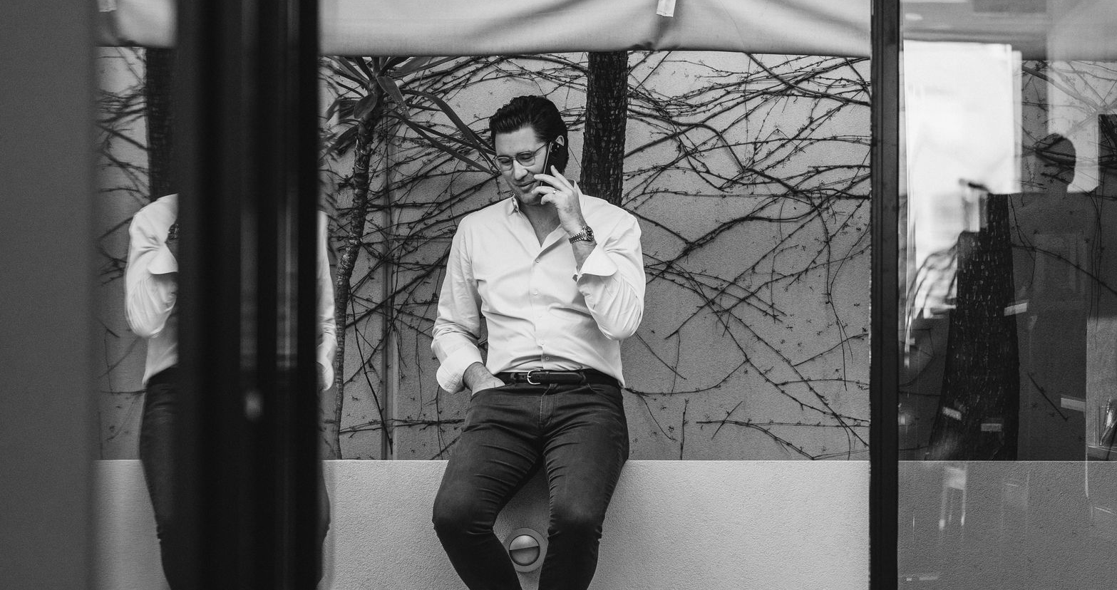 Man leaning against window, talking on phone, legs crossed. Black and white.