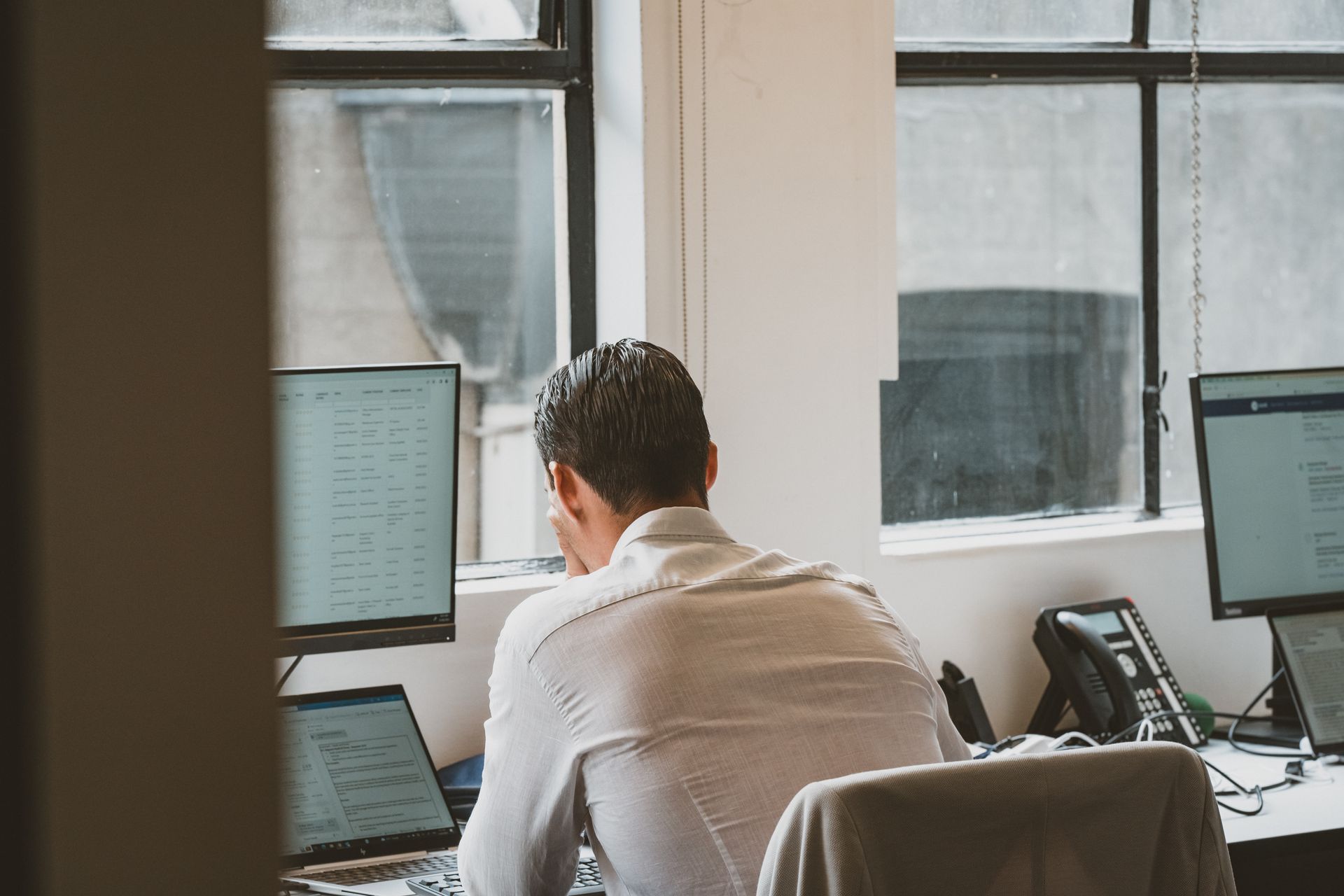 Man at desk with multiple computer screens and phone, working in an office setting.