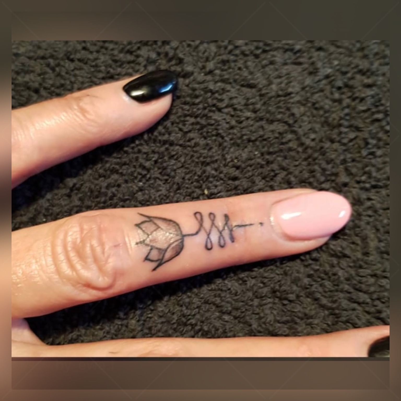 Eine Frau mit schwarzen Nägeln hat eine kleine Tätowierung auf ihrem Daumen.