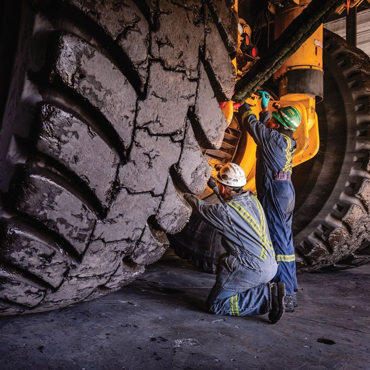 Two Heavy Duty Mechanics in safety gear inspecting a large, piece of machinery.