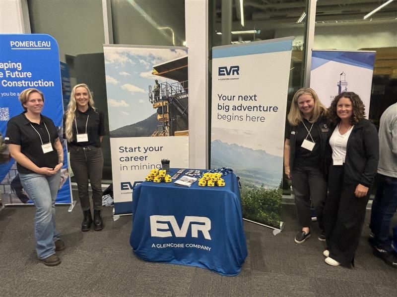 A female Haul Truck Operator wearing personal protective equipment operating heavy machinery, holding the steering wheel.