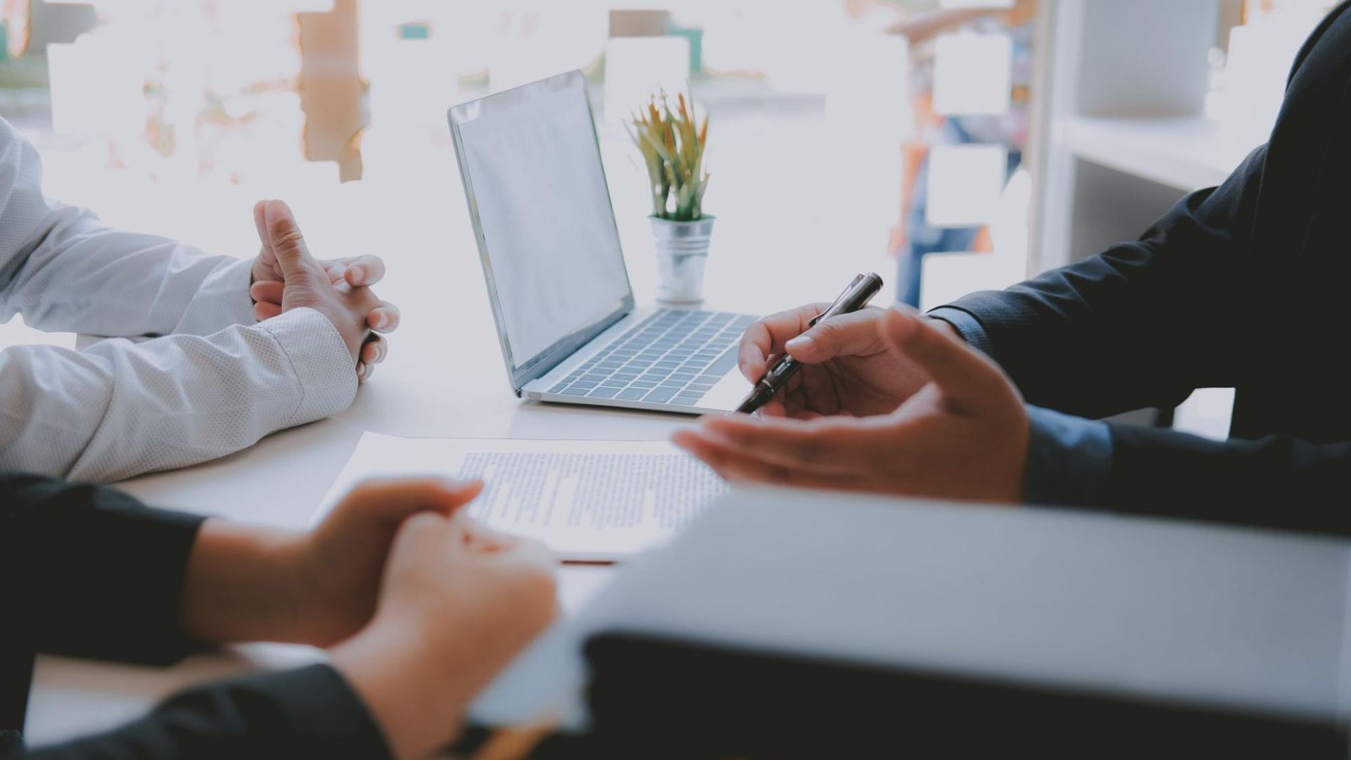 A group of lawyers are sitting at a table with a laptop and a pen.